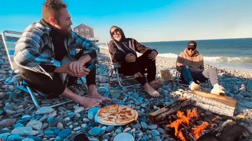 Men gathered around a beach campfire at golden hour